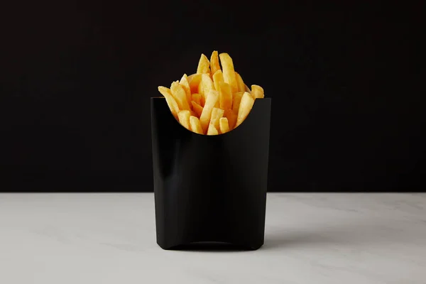 Caixa de batatas fritas na superfície de mármore branco isolado em preto — Fotografia de Stock