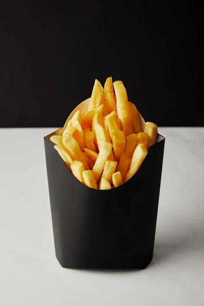 Close-up shot of box of french fries on white marble surface isolated on black — Stock Photo