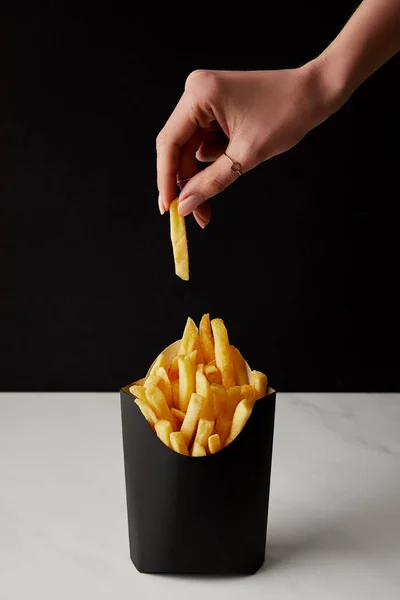 Mujer sacando patatas fritas de caja aislada en negro - foto de stock