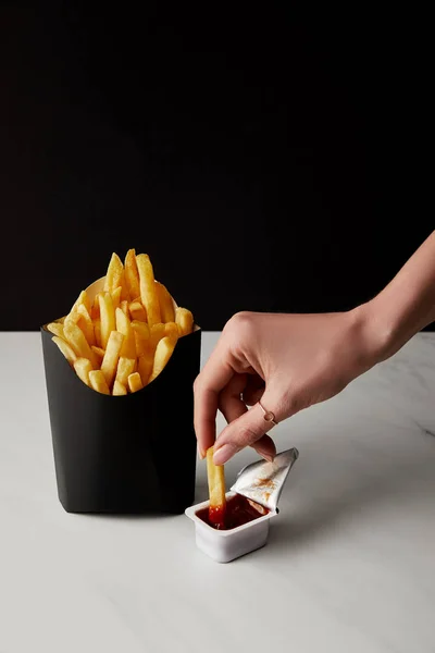 Corte tiro de mulher derramando francês fritar em ketchup isolado em preto — Fotografia de Stock