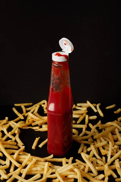 Bottiglia di ketchup circondata da patatine fritte isolate su nero — Foto stock