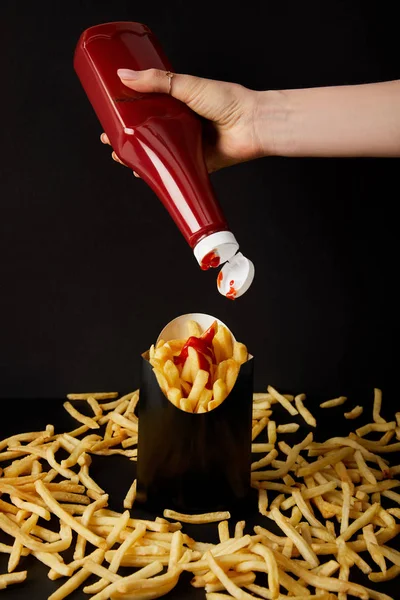 Cropped shot of woman pouring ketchup on french fries isolated on black — Stock Photo