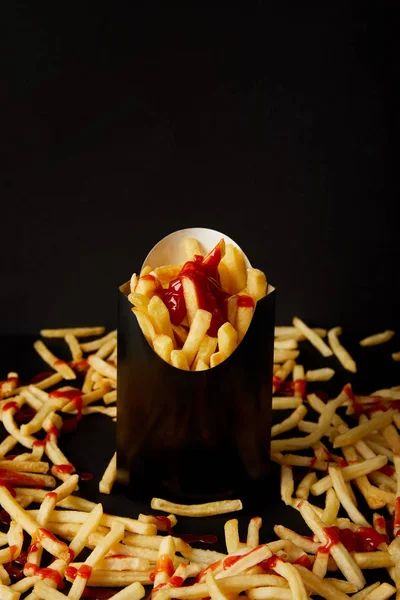 Close-up shot of french fries in black box surrounded with messy fries on tabletop isolated on black — Stock Photo