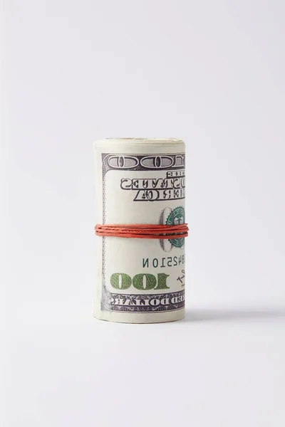Рулон долларов, привязанный резиновой лентой на белой поверхности — стоковое фото