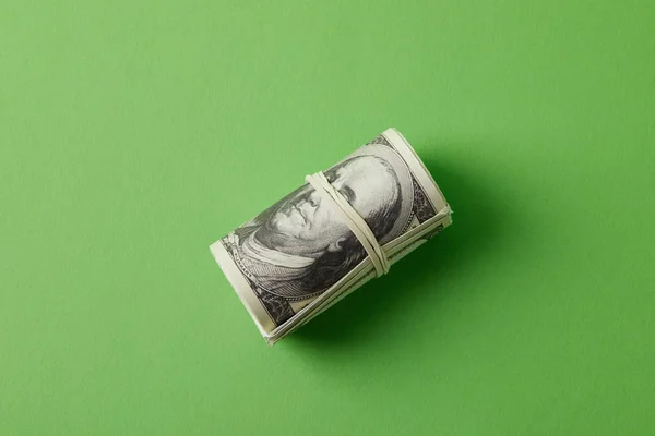 Top view of roll of dollars tied with rubber band on green — Stock Photo