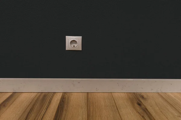 Single power socket in empty wall over wooden floor — Stock Photo