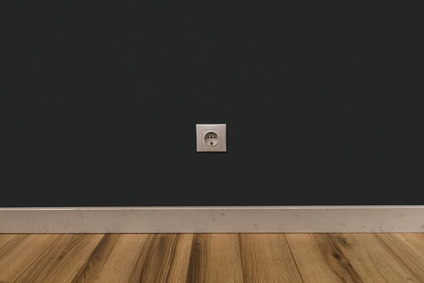 Single power socket in dark wall over wooden floor — Stock Photo