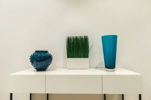 Blue vases and grass on white table by wall — Stock Photo