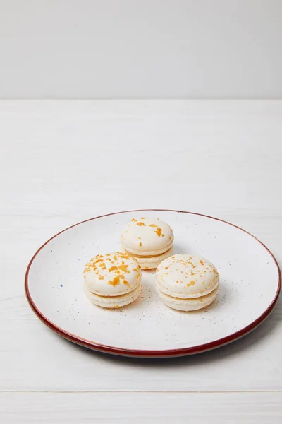 Primer plano de tres macarons en plato sobre mesa de madera blanca - foto de stock