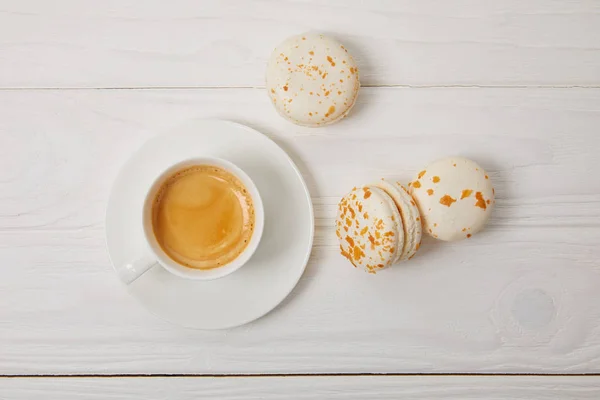 Draufsicht auf Kaffeetasse und drei Macarons auf weißem Holztisch — Stockfoto