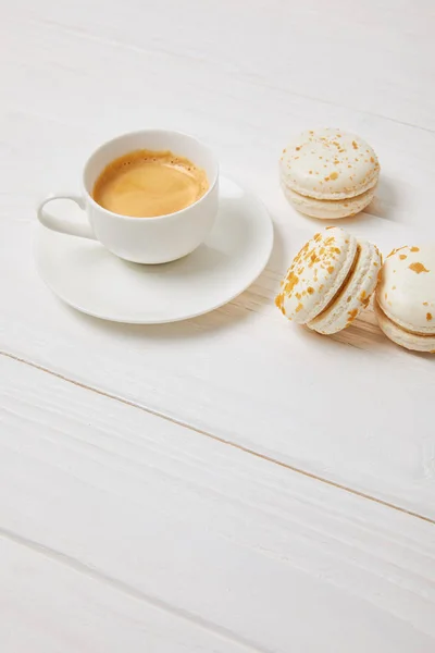 Tasse à café et trois macarons sur table en bois blanc — Photo de stock