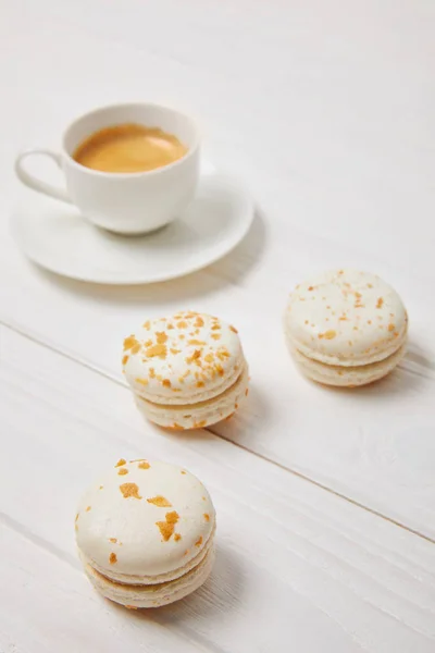 Nahaufnahme von Kaffeetasse und drei Macarons auf weißem Holztisch — Stockfoto