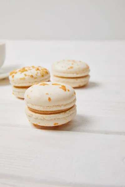 Vue partielle de tasse à café et trois macarons sur table en bois blanc — Photo de stock