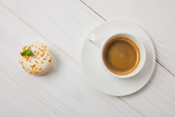 Top view of cup of coffee with saucer and macaroon on white wooden table — Stock Photo