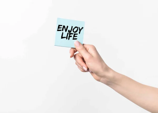 Partial shot of woman holding blue sticky note with Enjoy life inspiration, isolated n white — Stock Photo