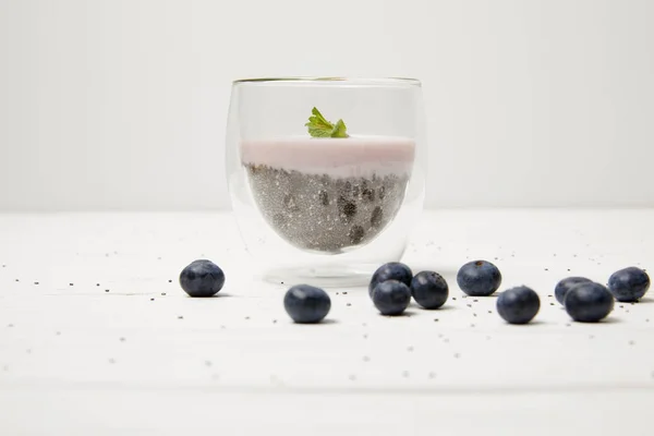 Vue rapprochée du pudding aux graines de chia avec des feuilles de menthe et des bleuets frais sur le dessus de table blanc — Photo de stock