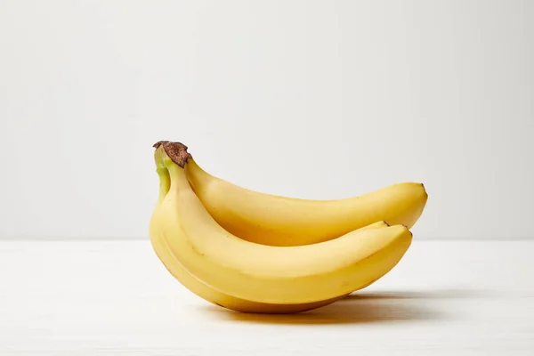 Vista de cerca de plátanos maduros sobre una mesa blanca sobre fondo gris - foto de stock