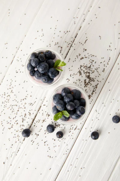 Top view of arranged chia puddings with fresh blueberries and mint on white wooden surface — Stock Photo
