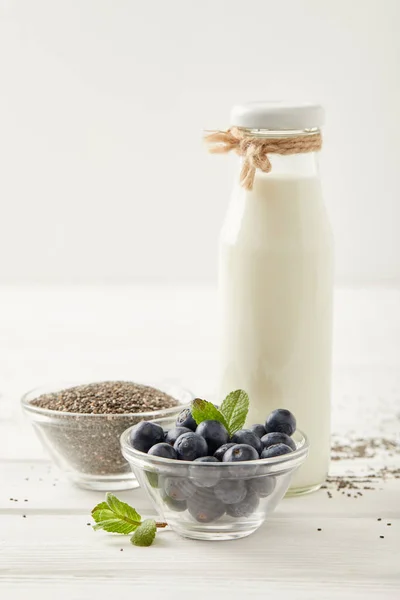 Nahaufnahme einer Flasche Milch, Blaubeeren und Chia-Samen zur Herstellung von Chia-Pudding auf einer weißen Holzplatte — Stockfoto