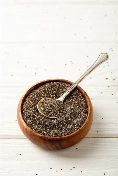 Vue rapprochée des graines de chia et cuillère dans un bol en bois sur la surface blanche — Stock Photo
