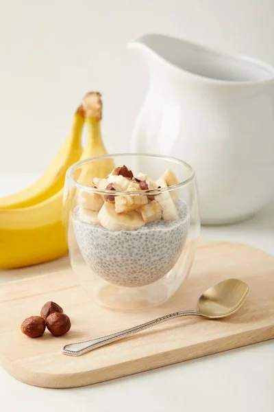 Vista de perto de pudim de semente de chia com pedaços de banana e avelãs em tábua de corte de madeira com colher — Fotografia de Stock