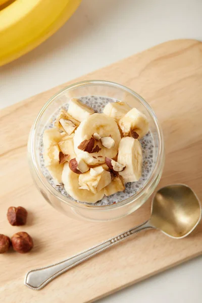 Vista superior do saboroso pudim de semente de chia com pedaços de banana e avelãs na mesa branca — Fotografia de Stock