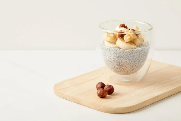 Close up view of tasty chia seed pudding with pieces of banana and hazelnuts on wooden cutting board on tabletop — Stock Photo