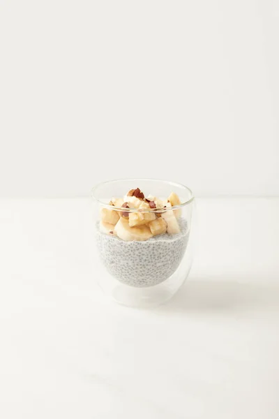 Close up view of tasty chia seed pudding with pieces of banana and hazelnuts on white tabletop — Stock Photo