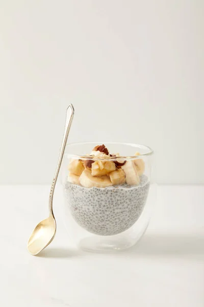 Vue rapprochée du savoureux pudding aux graines de chia avec des morceaux de banane et de noisettes sur le dessus de table blanc — Photo de stock