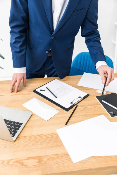 Vista parcial del hombre de negocios en el lugar de trabajo con cuadernos, bloc de notas y computadora portátil en la oficina - foto de stock