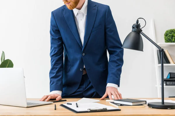 Vue partielle de l'homme d'affaires sur le lieu de travail avec ordinateur portable, ordinateurs portables et bloc-notes dans le bureau — Photo de stock