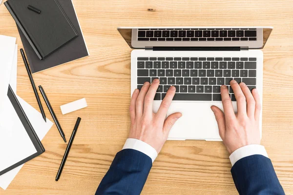 Cropped shot of businessman working on laptop at workplace with notebooks — Stock Photo