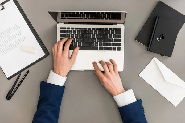 Cropped shot of businessman working on laptop at workplace with papers — Stock Photo