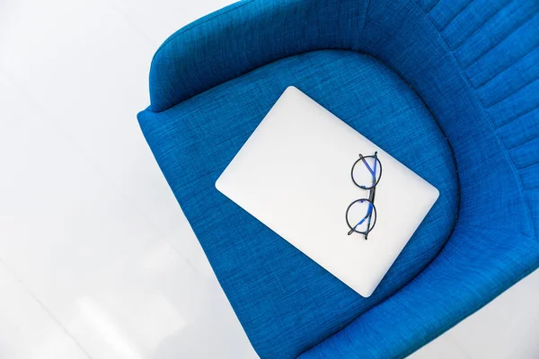 Vue du dessus de l'ordinateur portable et des lunettes sur chaise bleue — Photo de stock
