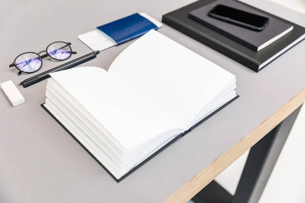 Close up view of arranged pile of empty opened notebook, eyeglasses, passport and ticket at workplace — Stock Photo