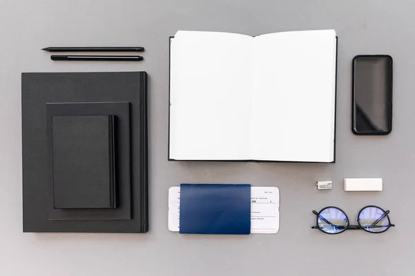 Top view of arranged pile of black notebooks, smartphone, empty opened notebook, passport and ticket at workplace — Stock Photo