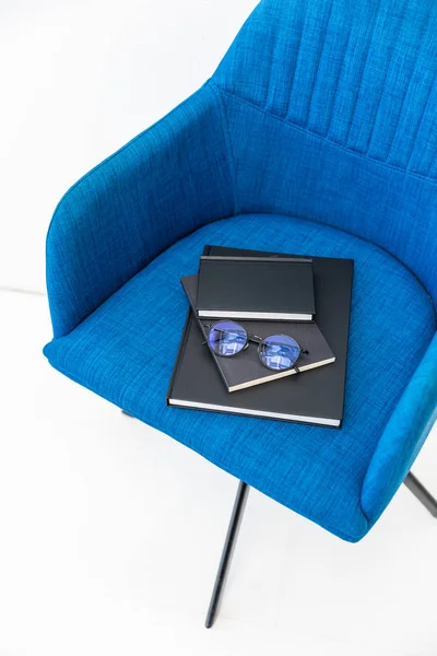 Close up view of pile of black notebooks and eyeglasses on blue chair on white background — Stock Photo