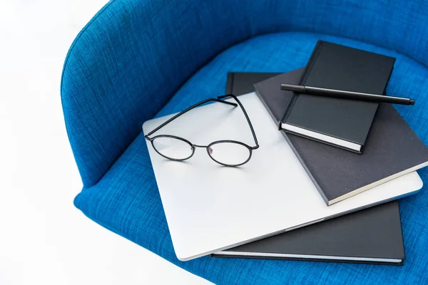 Vista de cerca de la computadora portátil, cuadernos negros y anteojos en la silla azul aislado en blanco - foto de stock