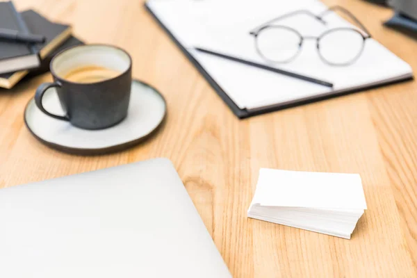 Selective focus of cup of coffee, eyeglasses, documents and blank cards at workplace in office — Stock Photo