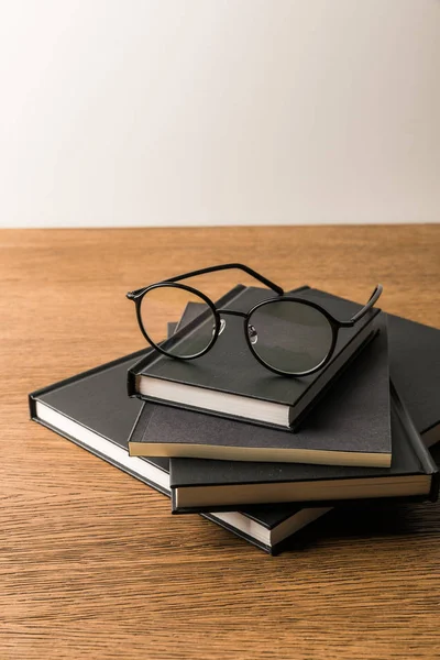 Close up view of pile of black notebooks and eyeglasses on wooden tabletop — Stock Photo