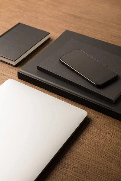 Vista de cerca de la computadora portátil, pila de cuadernos negros y teléfono inteligente en la mesa de madera — Stock Photo