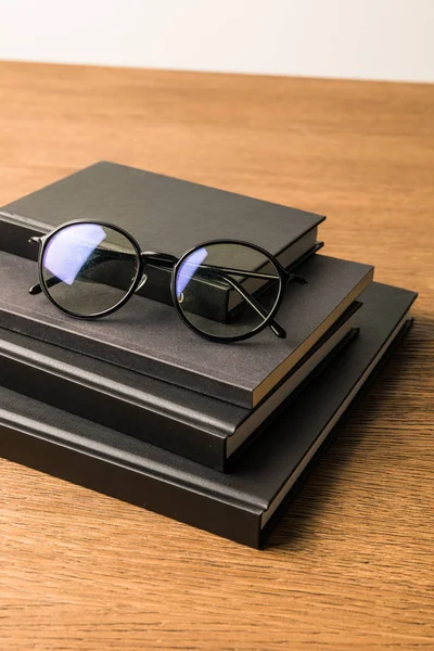 Close up view of pile of black notebooks and eyeglasses on wooden tabletop — Stock Photo