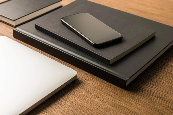 Close up view of laptop, pile of black notebooks and smartphone on wooden tabletop — Stock Photo