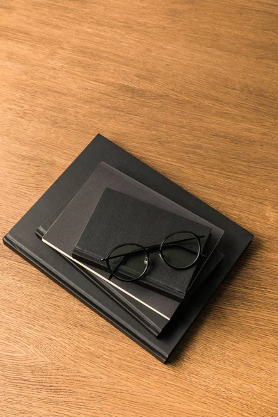 Top view of pile of black notebooks and eyeglasses on wooden tabletop — Stock Photo