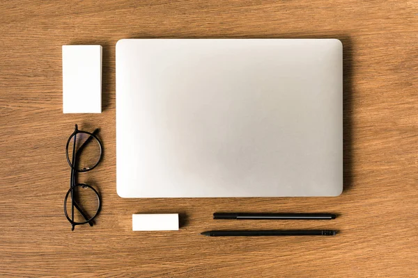 Acostado plano con portátil arreglado, anteojos, tarjetas en blanco, pluma y lápiz en la mesa de madera - foto de stock