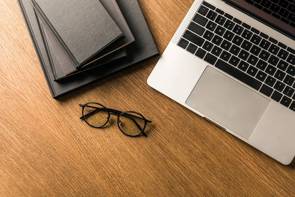 Draufsicht auf einen Stapel schwarzer Notizbücher, Laptops und Brillen auf einer hölzernen Tischplatte — Stockfoto