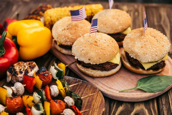 Hamburgers with flags and vegetables cooked outdoors on grill — Stock Photo