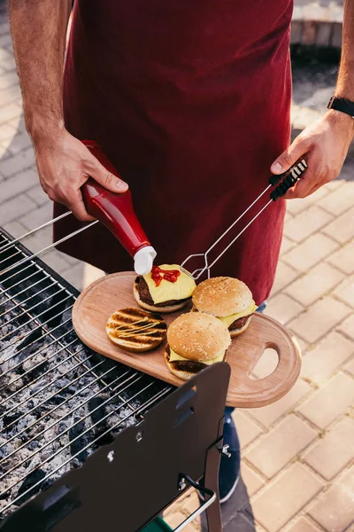 Шеф-повар добавляет кетчуп в бургеры на гриле для барбекю на открытом воздухе — стоковое фото