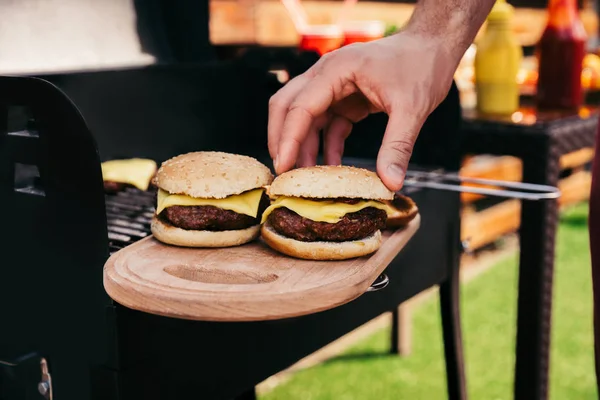 Человек кладет булочку на мясо гамбургеров на гриле для барбекю на открытом воздухе — стоковое фото