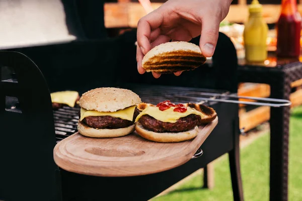 Chef sirviendo hamburguesas cocinadas al aire libre en tablero de madera - foto de stock